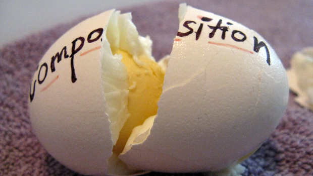 A photo of a hard-boiled egg, smashed in half. COMPOSITION is written in black ink on the eggshell.