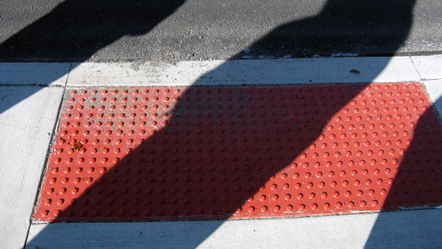 Photo of shadows across a red sidewalk curb cut