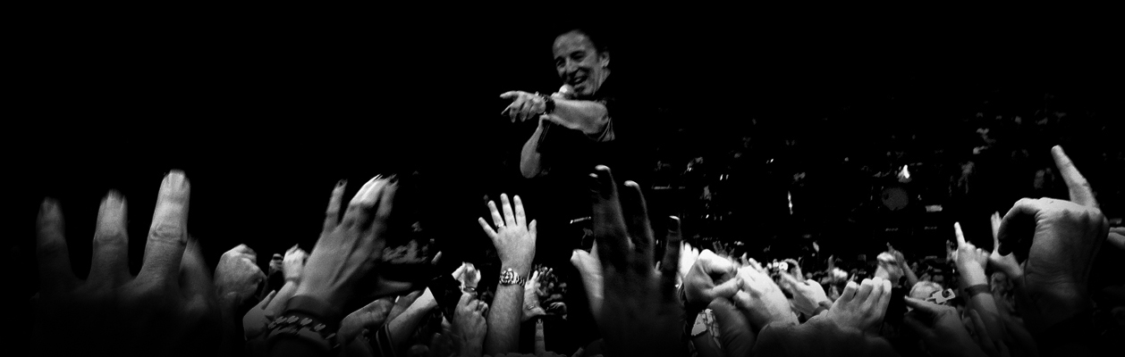 black and white photo of Bruce Springsteen standing in on a riser pointing to fans