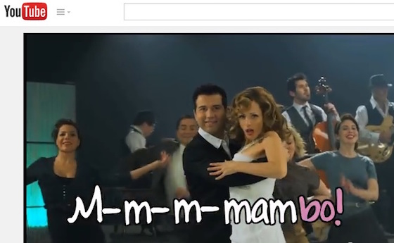 A man and woman are dancing the mambo and looking to the camera. The dynamic visual text is bubbled, mostly white, and says “M-m-m-mambo!” with hyphens in between each m. The last syllable, “bo!” is in pink.
