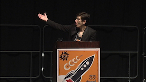 Linda Adler-Kassner standing behind the podium at Houston CCCC, gesturing behind her and to her right