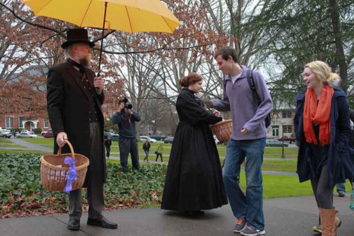 white man and woman dressed in old-style clothes greet pedestrians on a sidewalk