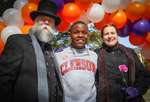 man and woman dressed in old-style clothes posing for photograph with Clemson student; baloons in background