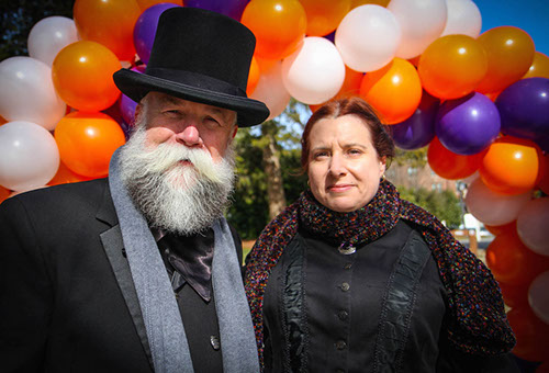 man and woman dressed in old-style clothes posing for photograph in front of balloons