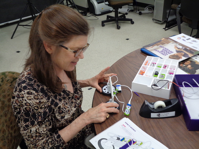 Leslie holds onto some littleBits as she looks at print instructions sitting on the table