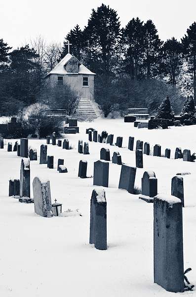 a black and white image of a graveyard in winter with a house in the background