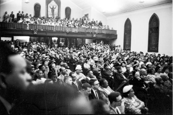 a crowded interior of a church, with pews and balcony filled with people; black and white