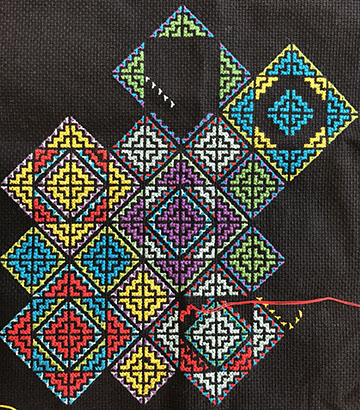 Black fabric featuring multicolored and differently sized squares of cross-stitch