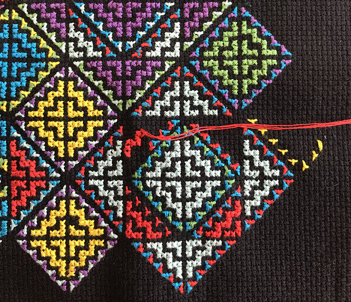Close up of black textile with a cross-stitch pattern in progress