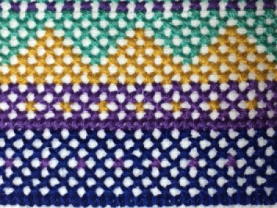 A geometric cross-stich pattern with purple, indigo, gold, and teal stitching