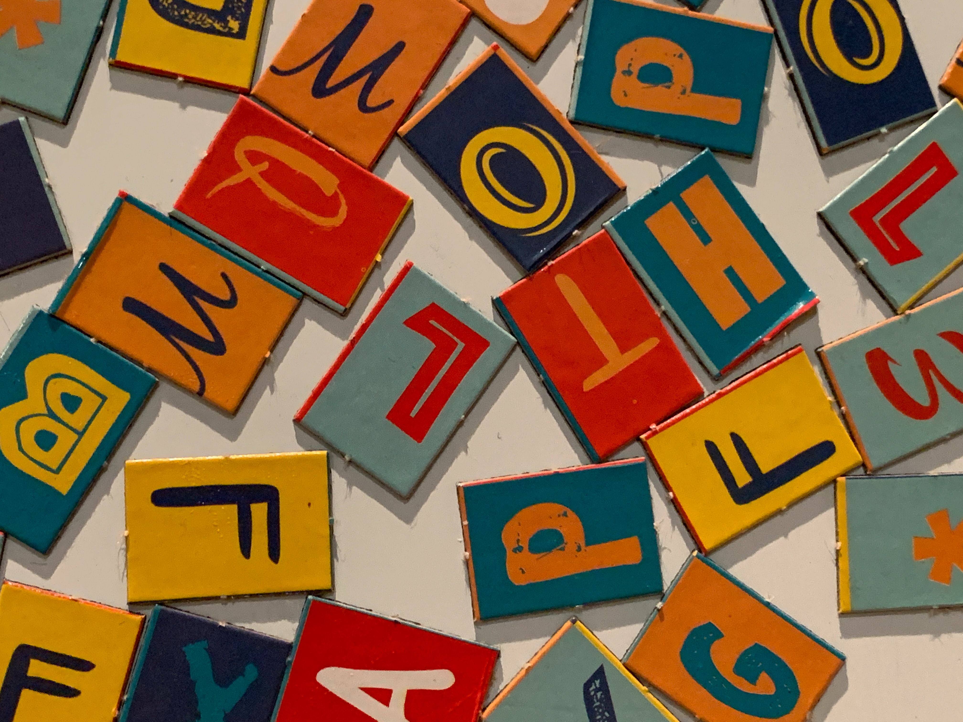 Uppercase letters written on red, orange, blue, and yellow tiles displayed in a disorganized pile