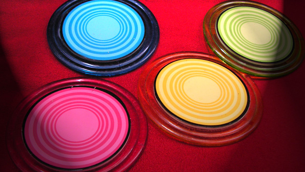 Four coasters -- blue, pink, yellow, and green -- sit on a red chair.
