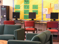 A row of computer stations in the back of a room. In front of the stations are several couches, in a lounge-like area.