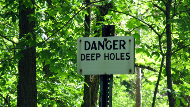 A white sign in the woods reads DANGER - DEEP HOLES.