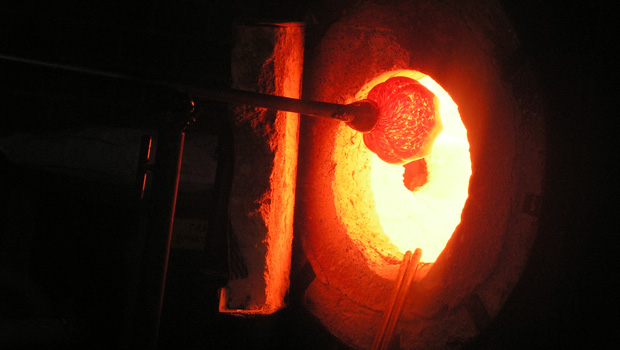 A dark photo of rounded glass (bright orange)  entering a kiln