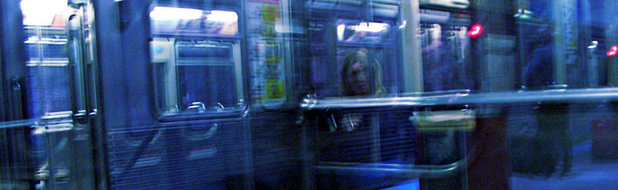 A blurred photo of a woman on an El train in Chicago. The photo is tinted blue and depicts the nside of a train car. The blurriness suggests that the car is moving.