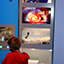 Photograph from the exhibition for the Xbox 360 game console: blue background with screen shots from four video games and a young person holding a telephone and viewing a separate screen with a game being displayed.