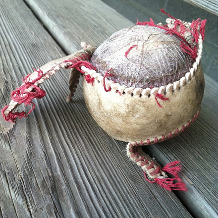 An old baseball with its stitches frayed and removed and half of the cover peeled back to reveal the tightly-bound twine beneath.