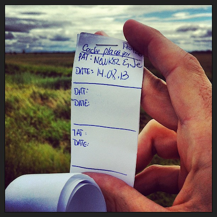 A close-cropped photo of a clean geocache log (one that has not been signed) with a grassy green field in the background.