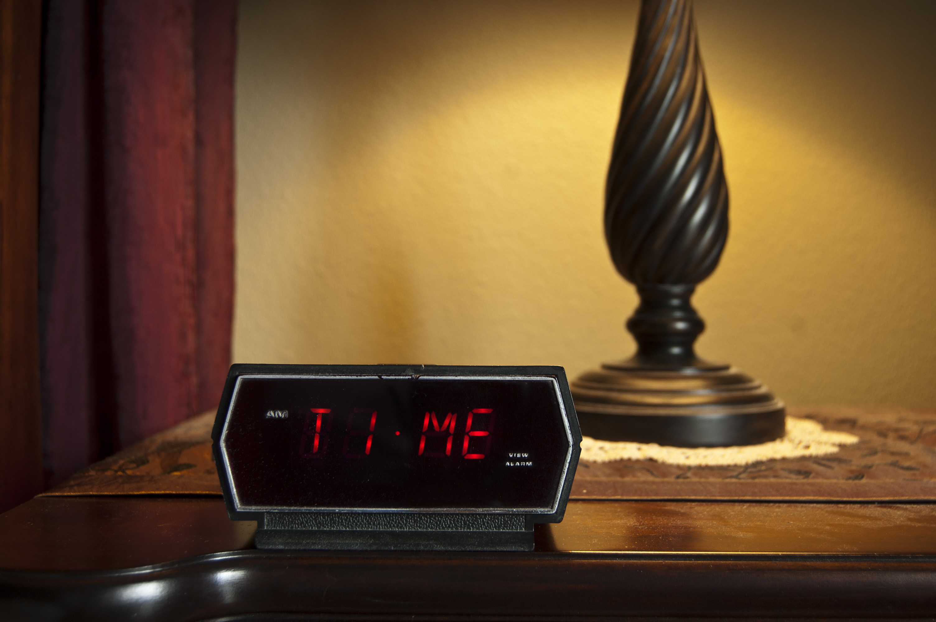 bedside table with lamp and digital clock with red numbers spelling TIME