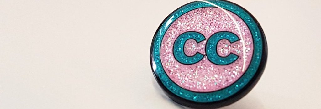 Light pink background, close up photo of glittery lapel pin with Creative Commons logo.
