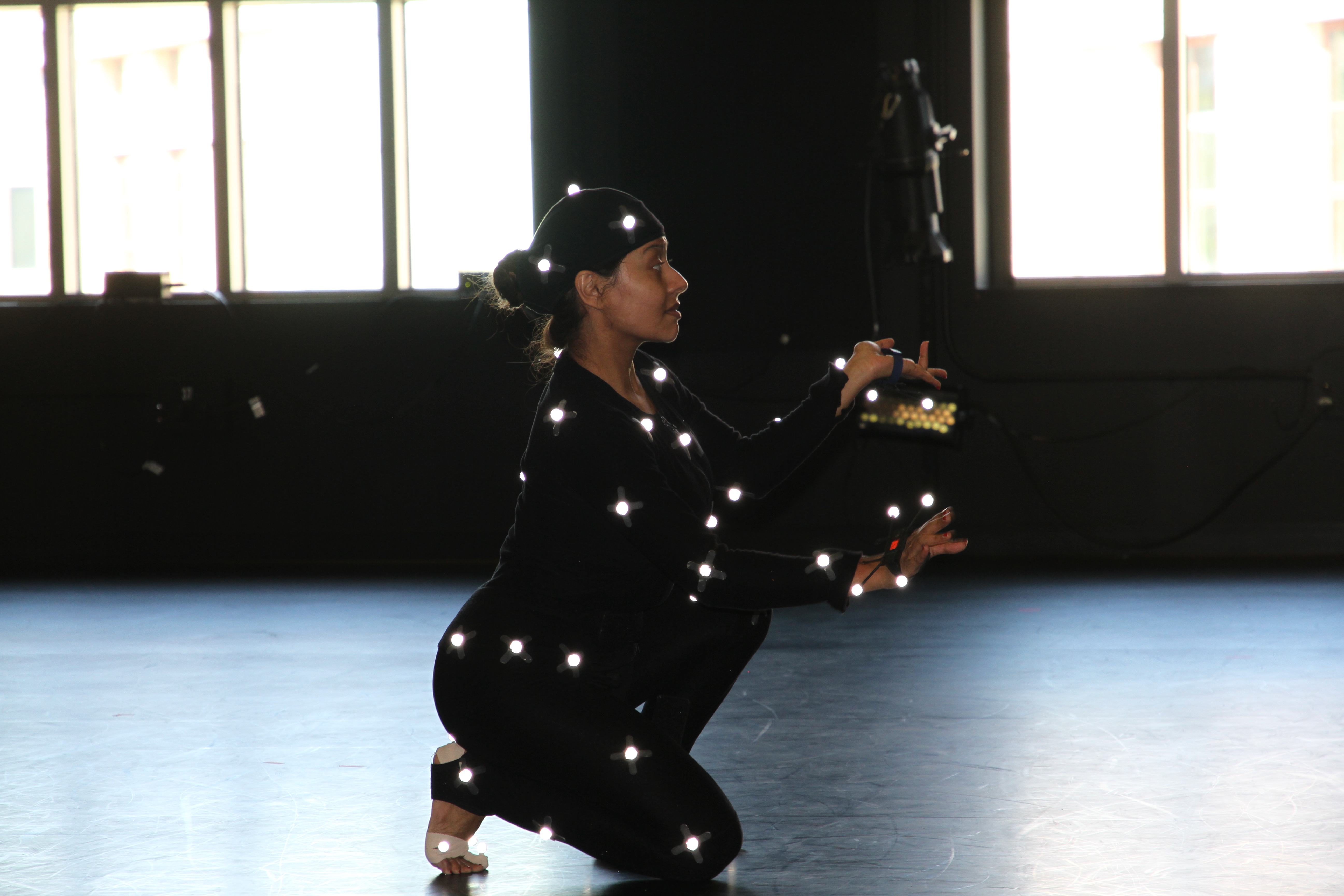 woman wearing black dancing, on her knee; small lights are placed on limbs, waist, and head