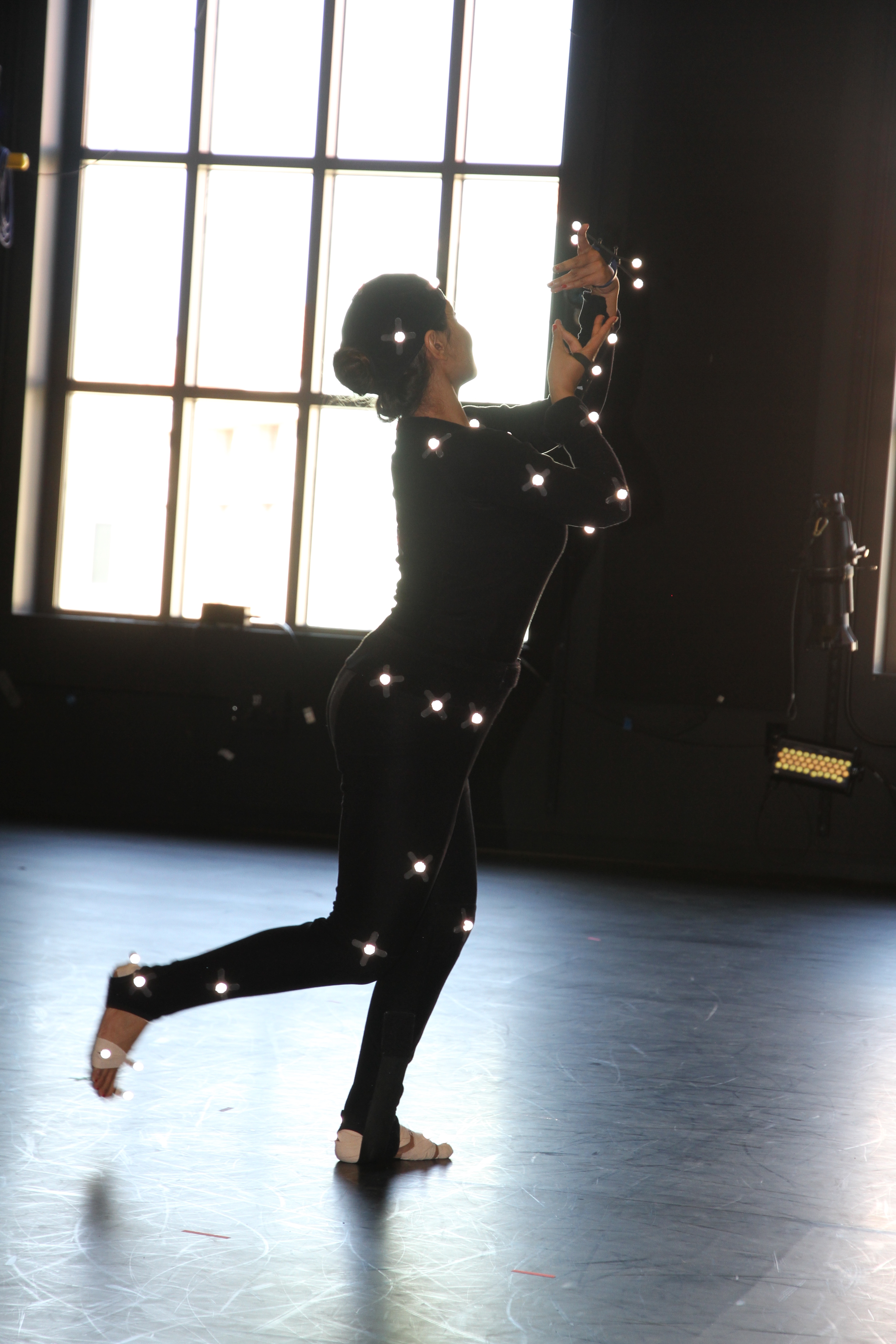 woman wearing black dancing; small lights are placed on limbs, waist, and head