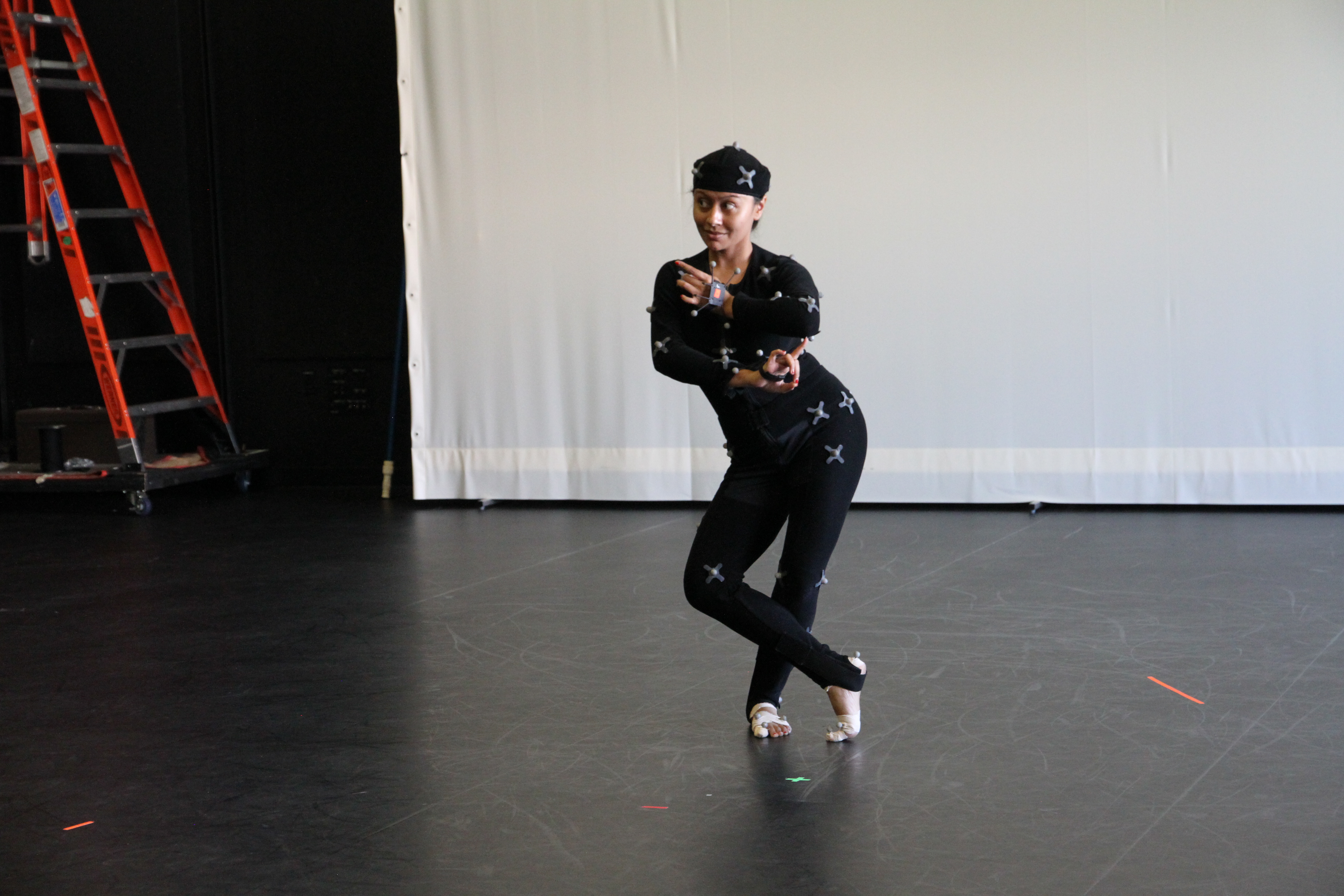 woman wearing black dancing in extreme s-curve; small lights are placed on limbs, waist, and head