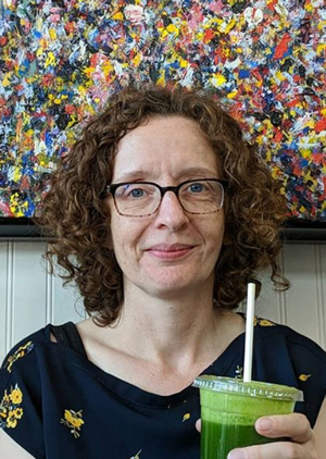 Julia Bleakney: face of woman with glasses and dark hair holding a green drink with a straw