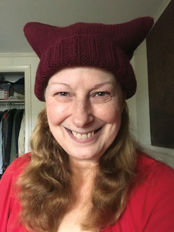 A photo shows a woman with light skin and a burgundy knit 'pussy hat.'