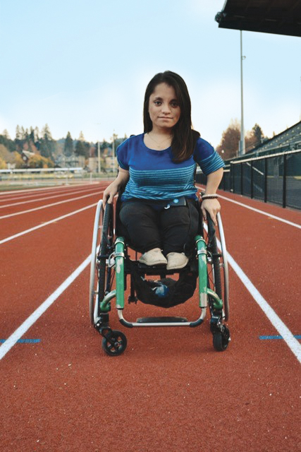 A photo shows a little person sitting in a wheelchair on a running track.