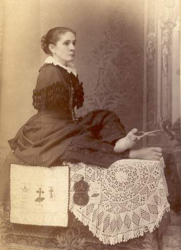 A sepia print showing a woman who has no arms. She is seated, using her toes to manipulate a pair of scissors.