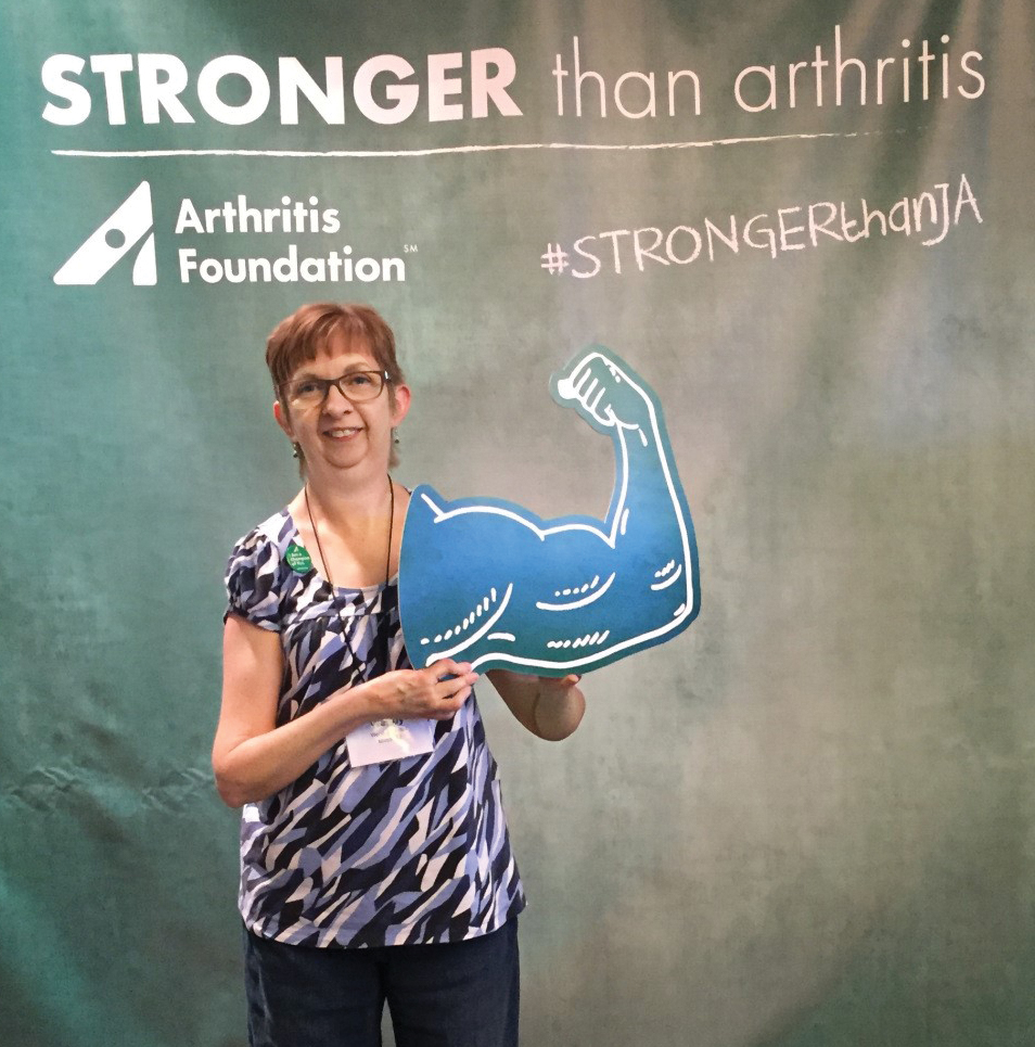 A photo shows a woman holding a flexed bicep cutout as she stands in front of a banner that reads: Stronger than arthritis.