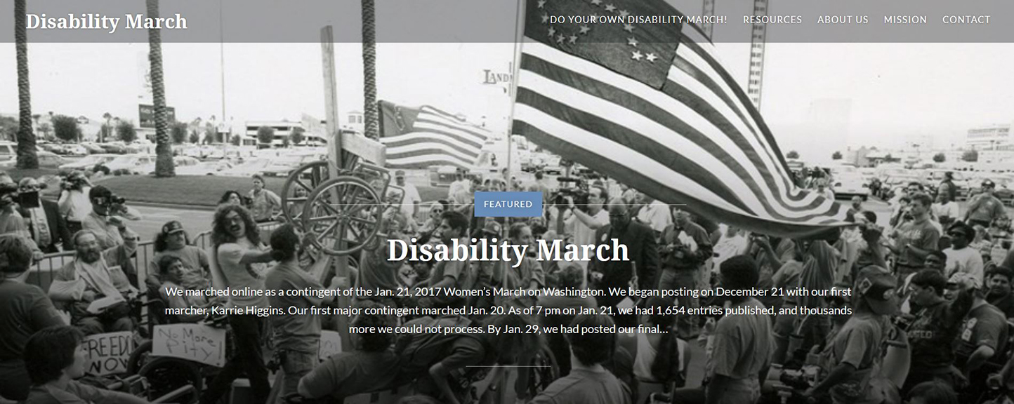 A black-and-white image shows a crowd of protestors, some in wheelchairs, holding up an American flag with a wheelchair outlined in stars. Some protestors hold signs and others a cross with a wheelchair attached to it.