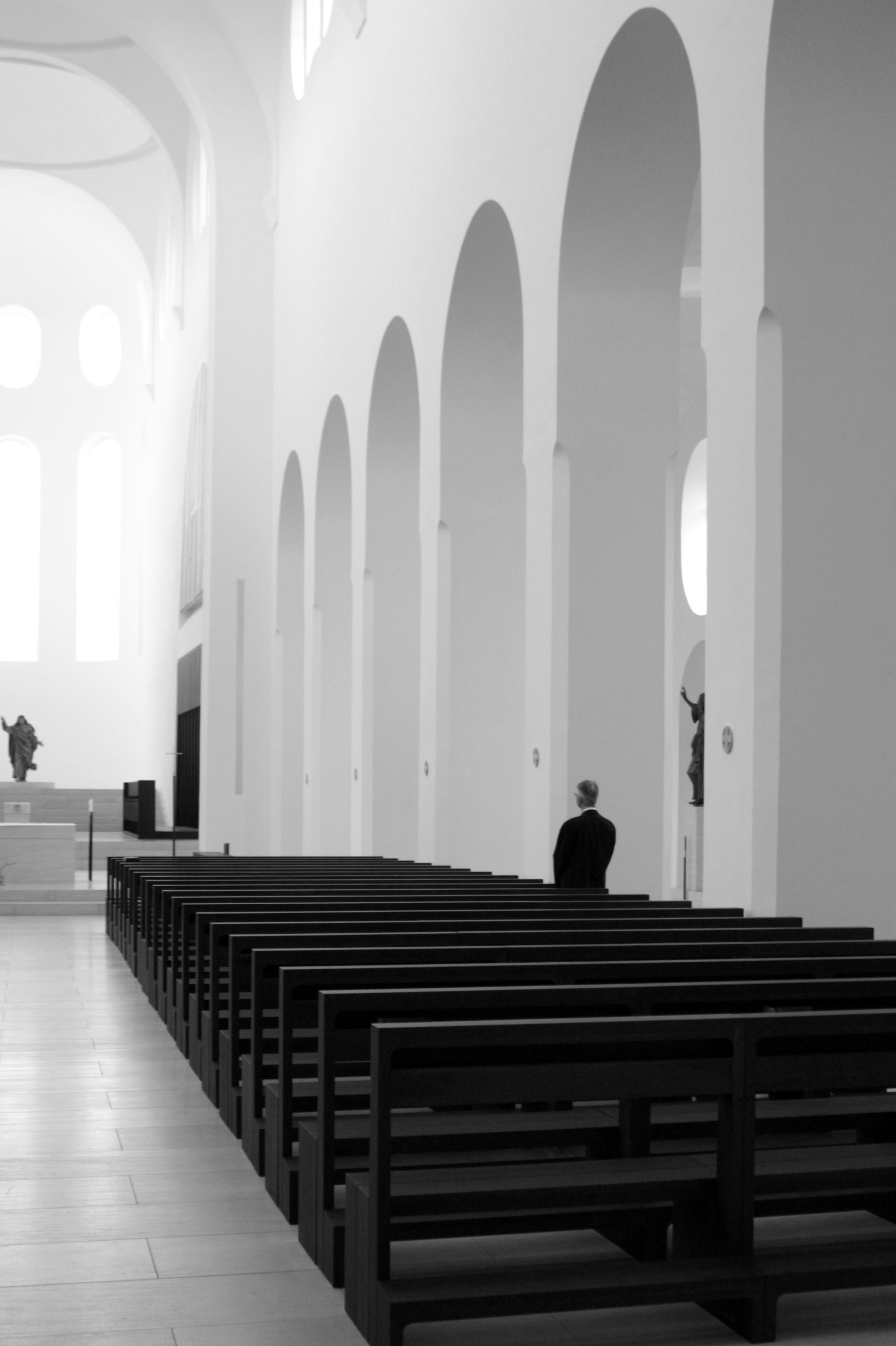 A solitary figure stands in a church with several tall archways