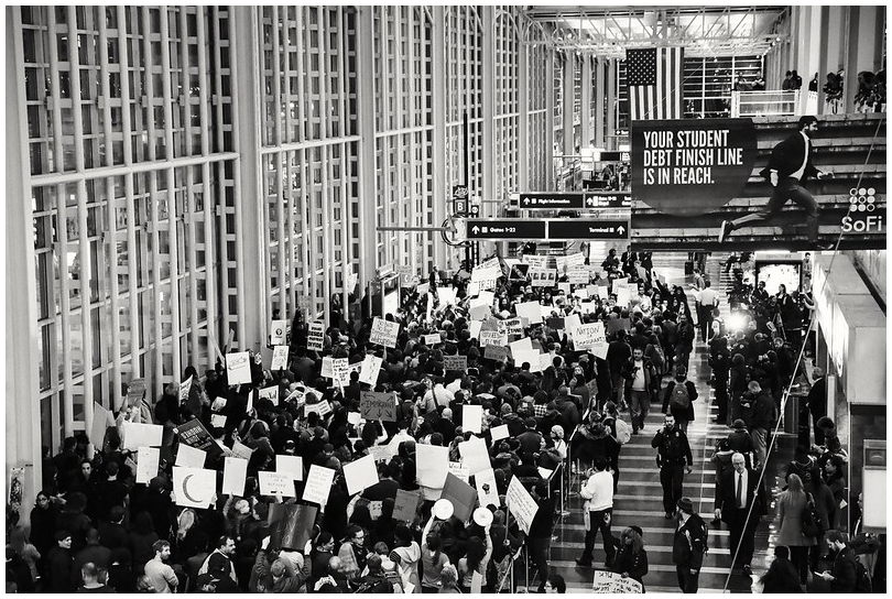 Large crowd holding protest signs, with a Student Debt Finish Line advertisement banner visible over the protestors.