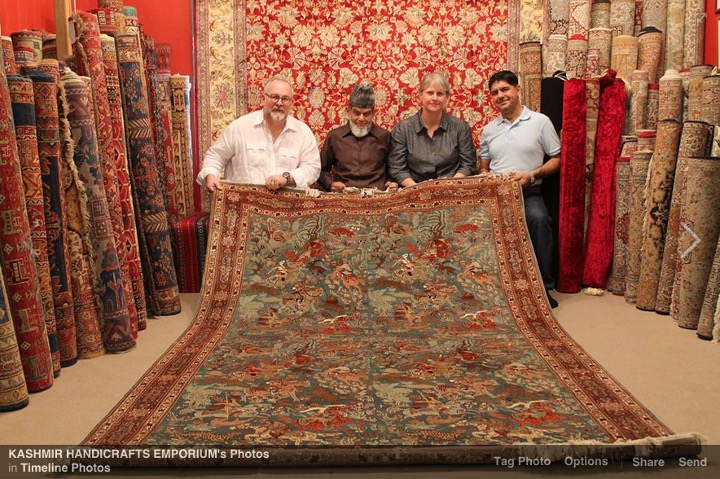 Three men and one woman sit holding a large silk rug