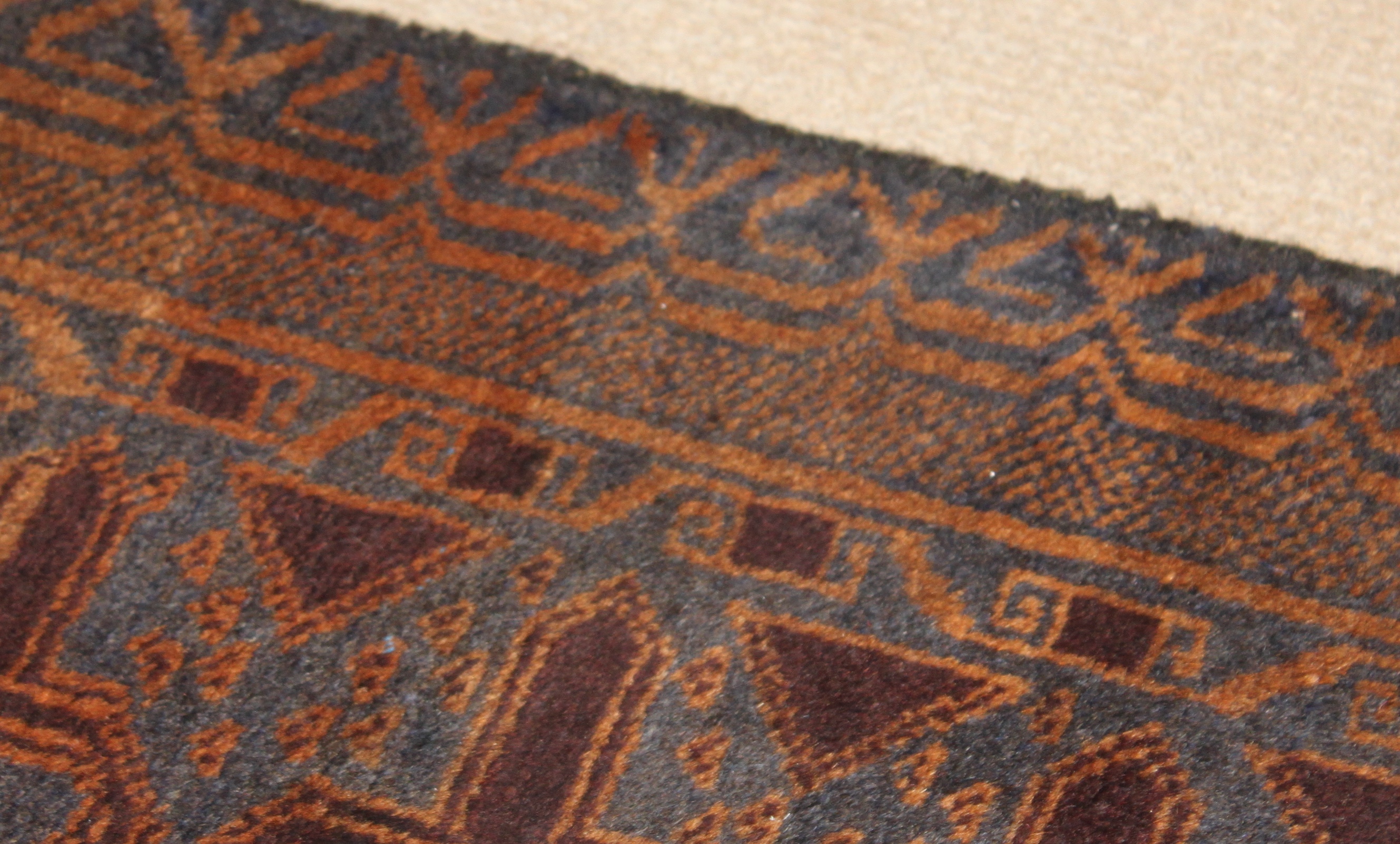 A rug with a blue background and orange and brown geometric patterns is photographed close up. Minor variations in the indigo color illustrate the variation called abrash.
