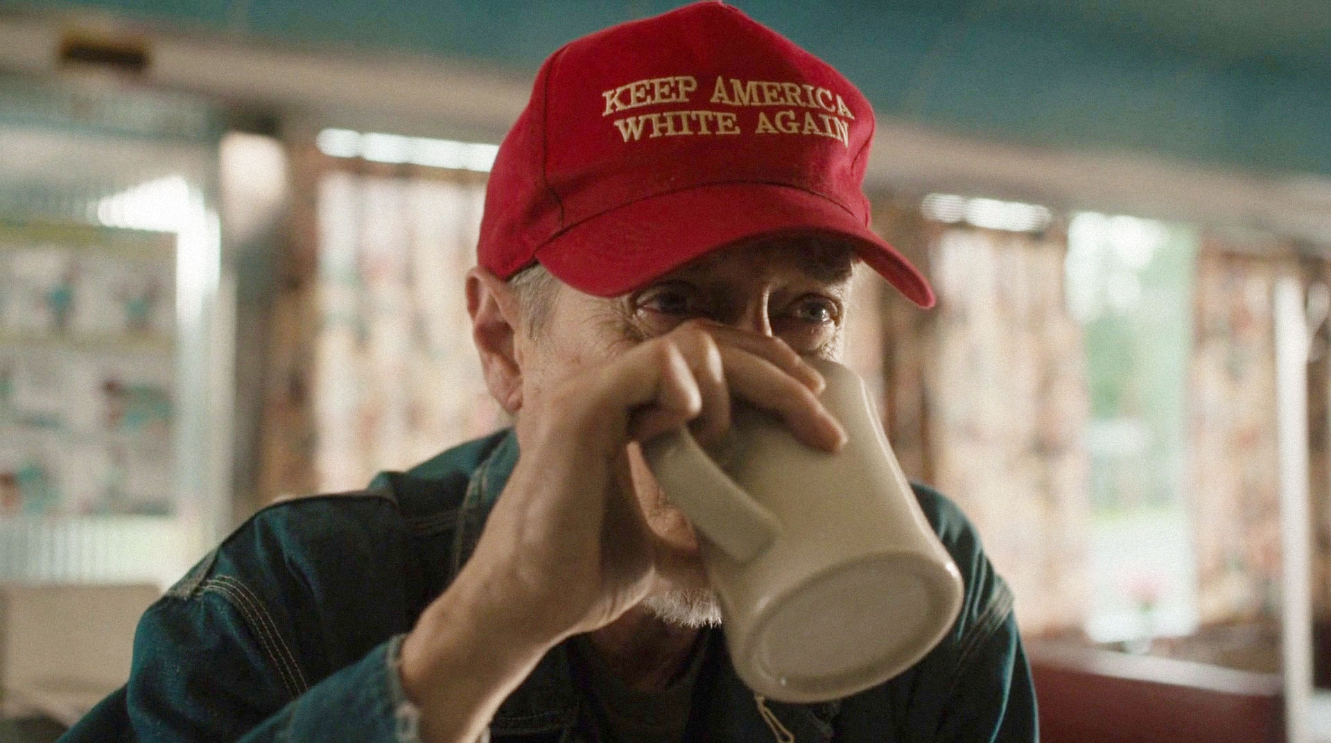 white man drinking coffee and wearing a red hat that says Keep America White Again