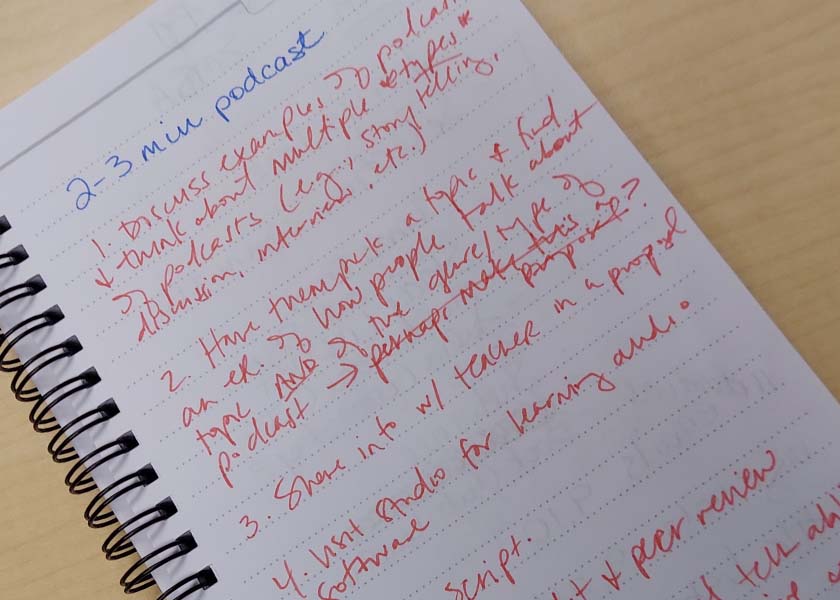 spiral notebook with text at top: 2-3 min podcast. lots of red cursive text below.
