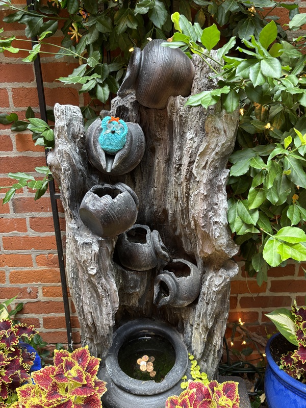 CC sitting on a garden fountain that looks like water flowing down broken cauldrons.