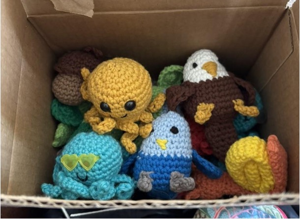 Various crochet creatures in different colors, including an octopus, eagle, snail, and acorn, sit in a cardboard box.