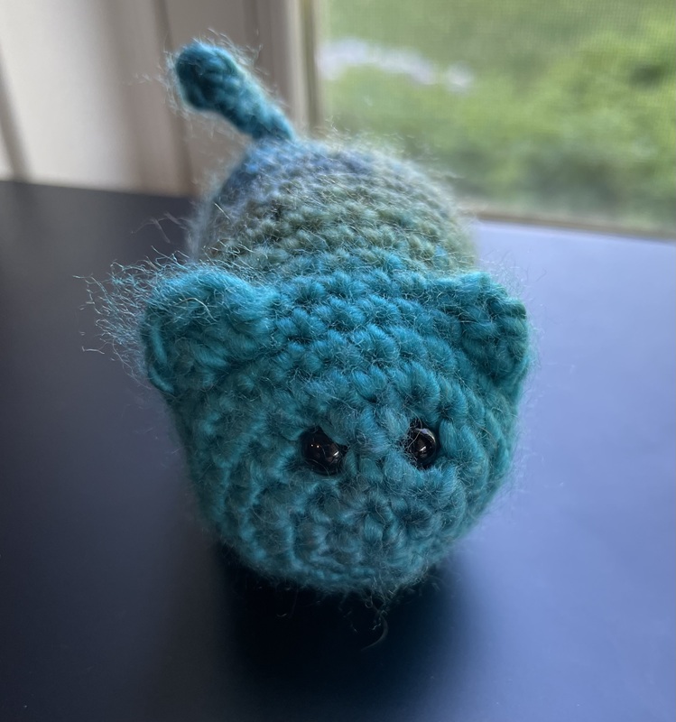 A crochet cat made of blue and green yarn in a round frame that served as the Instagram profile picture.