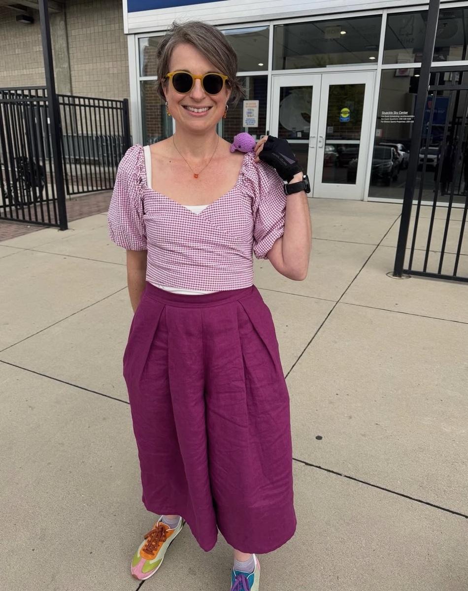 Jenn poses in a handmade purple outfit with a purple crochet whale on her shoulder.