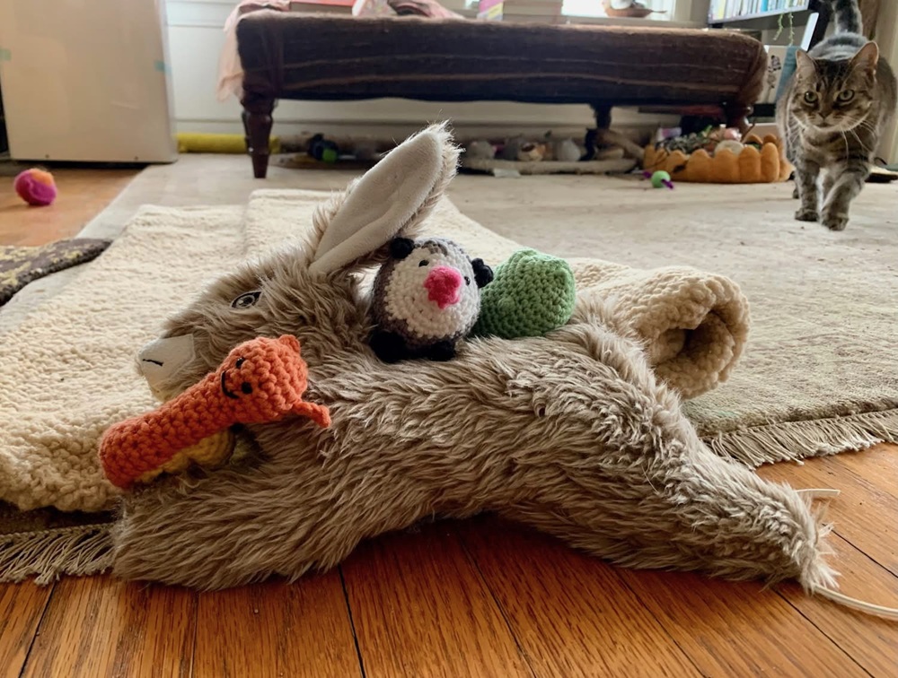 A light green crochet cat, a crochet possum, and a crochet snail rest on top of a brown fox cat toy.