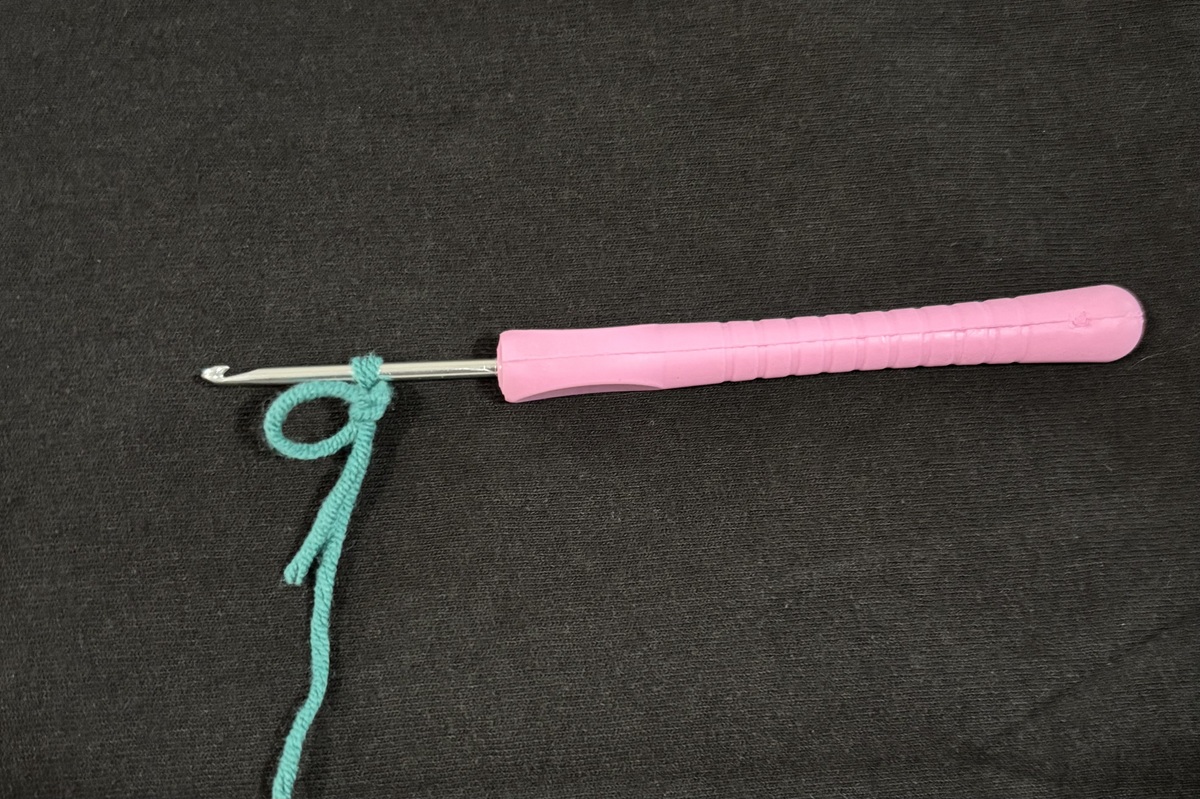 A purple crochet hook with one loop of blue yarn on top of a black background.