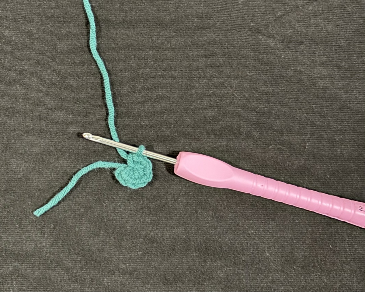 A purple crochet hook with a small circle of crocheted blue yarn on top of a black background.