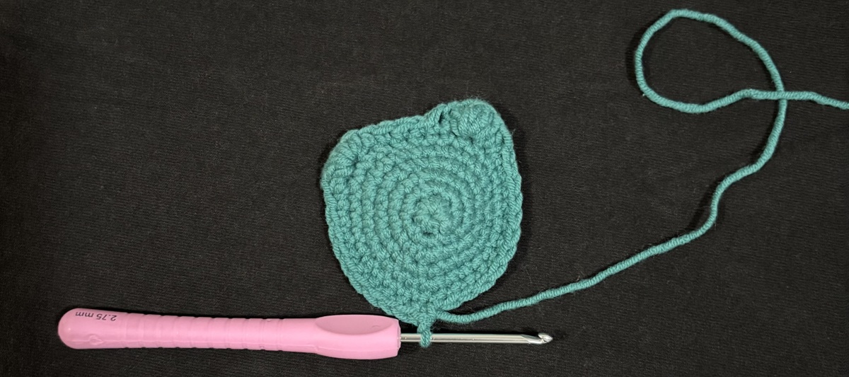 Banner Blue crochet in the shape of a cat's face attached to a purple crochet hook on a black background.