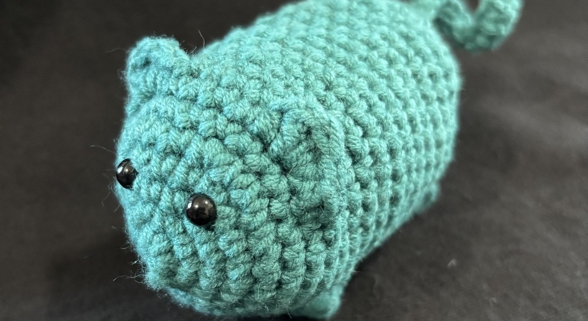 A completed blue crochet cat on a black background.