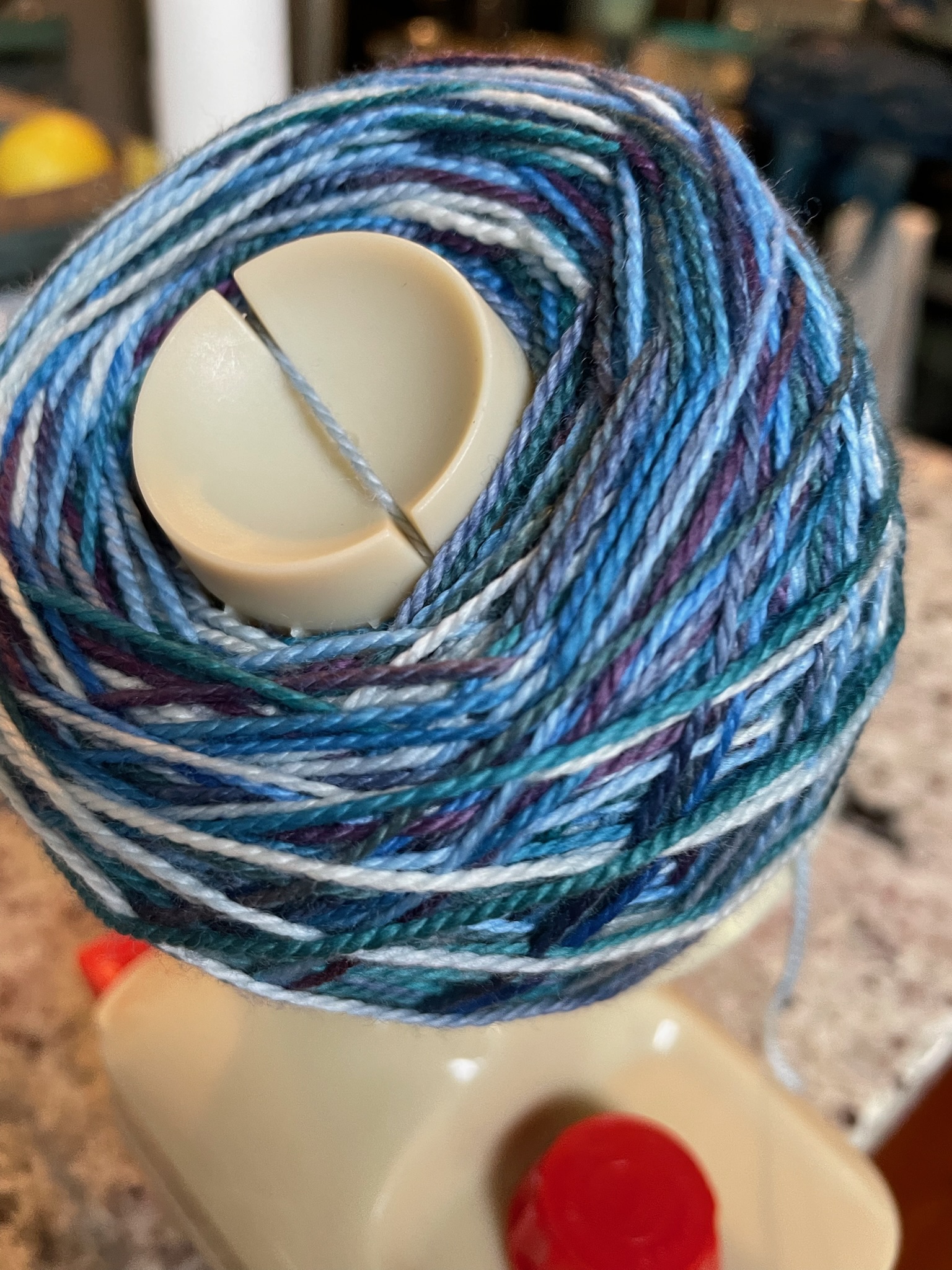 Blue, purple, and white yarn on a yarn winder.